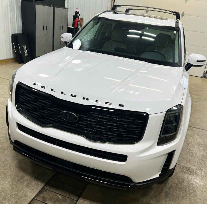 White SUV parked indoors, front view with black grille and roof rack on a wet concrete floor