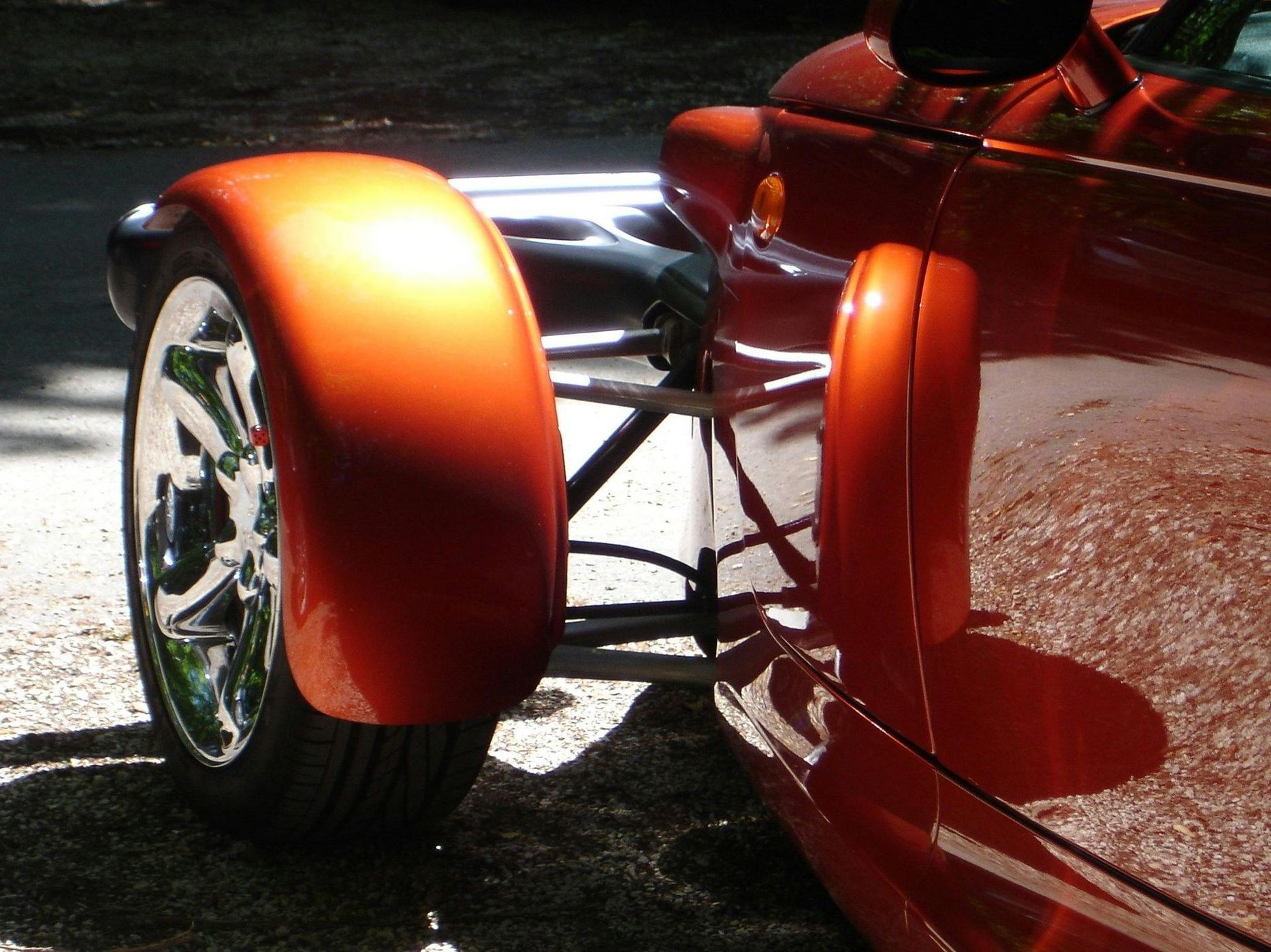 Orange vintage car's front fender and wheel, chrome rims, shiny paint, outdoor setting.