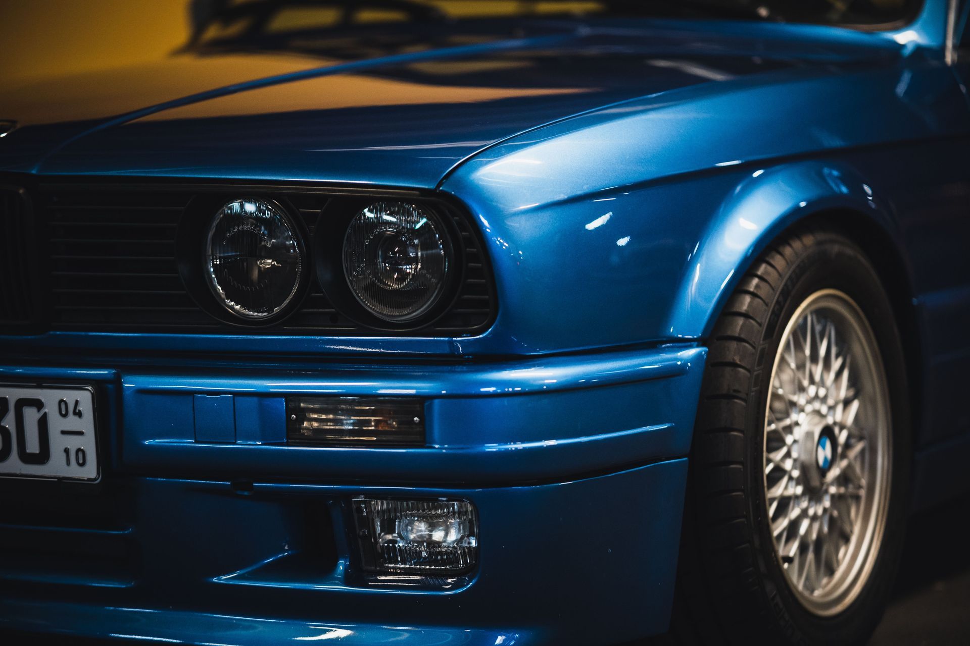 Close-up of a blue sports car front with round headlights and silver alloy wheel