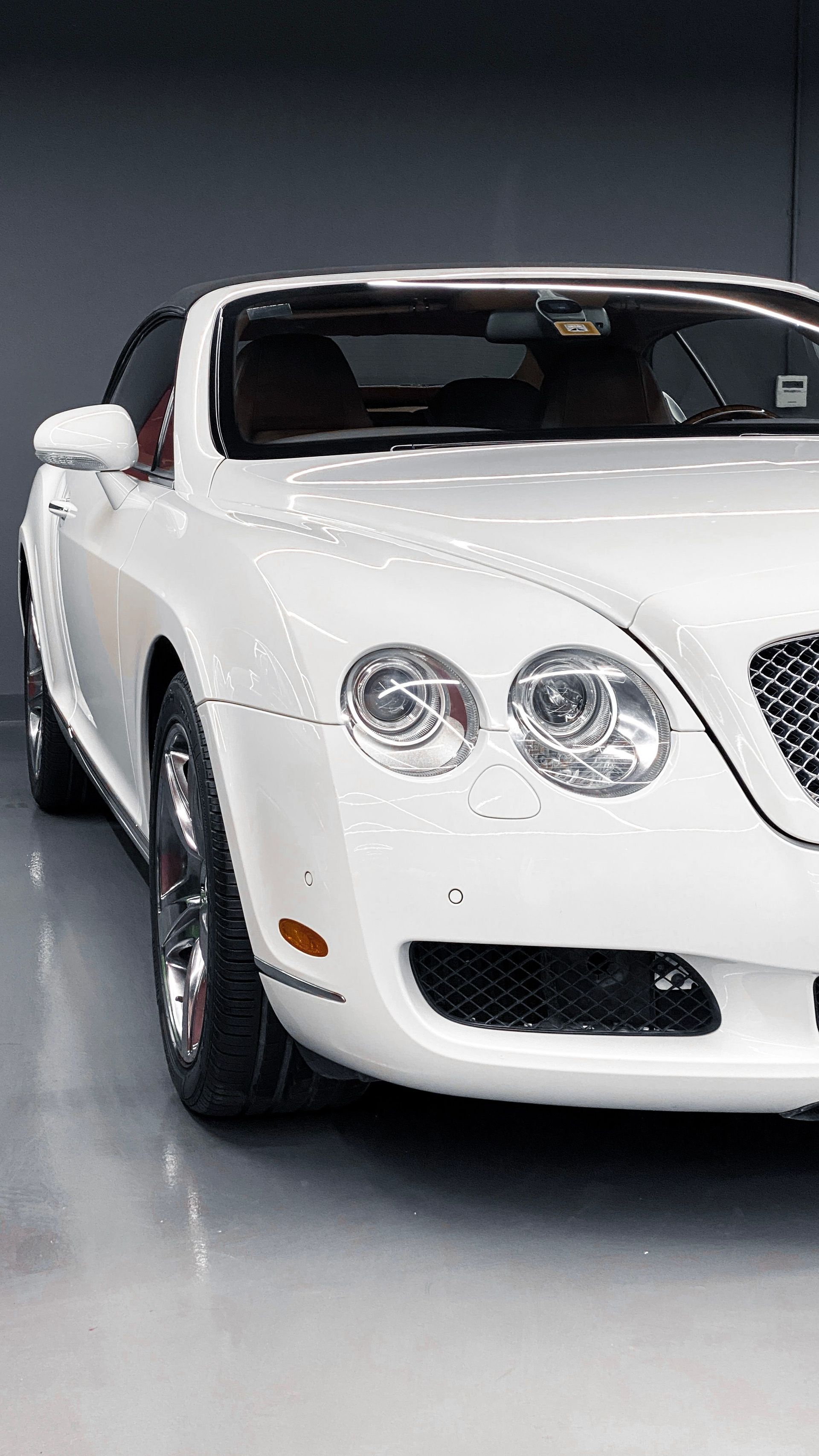 White luxury sports coupe in a studio, front-left view on a gray floor.