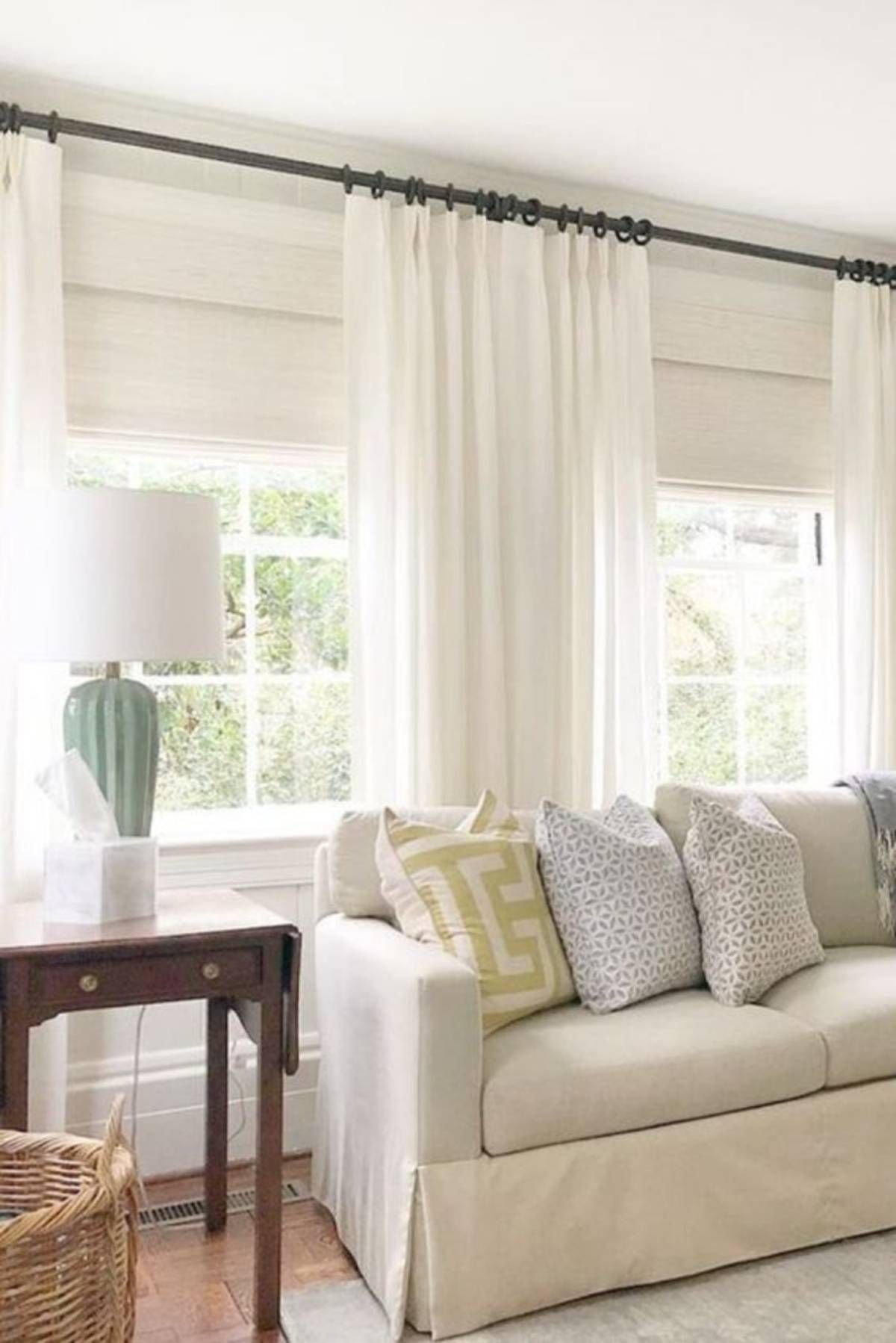 Living room windows with Provenance® woven wood shades layered under sheer white drapery panels as a