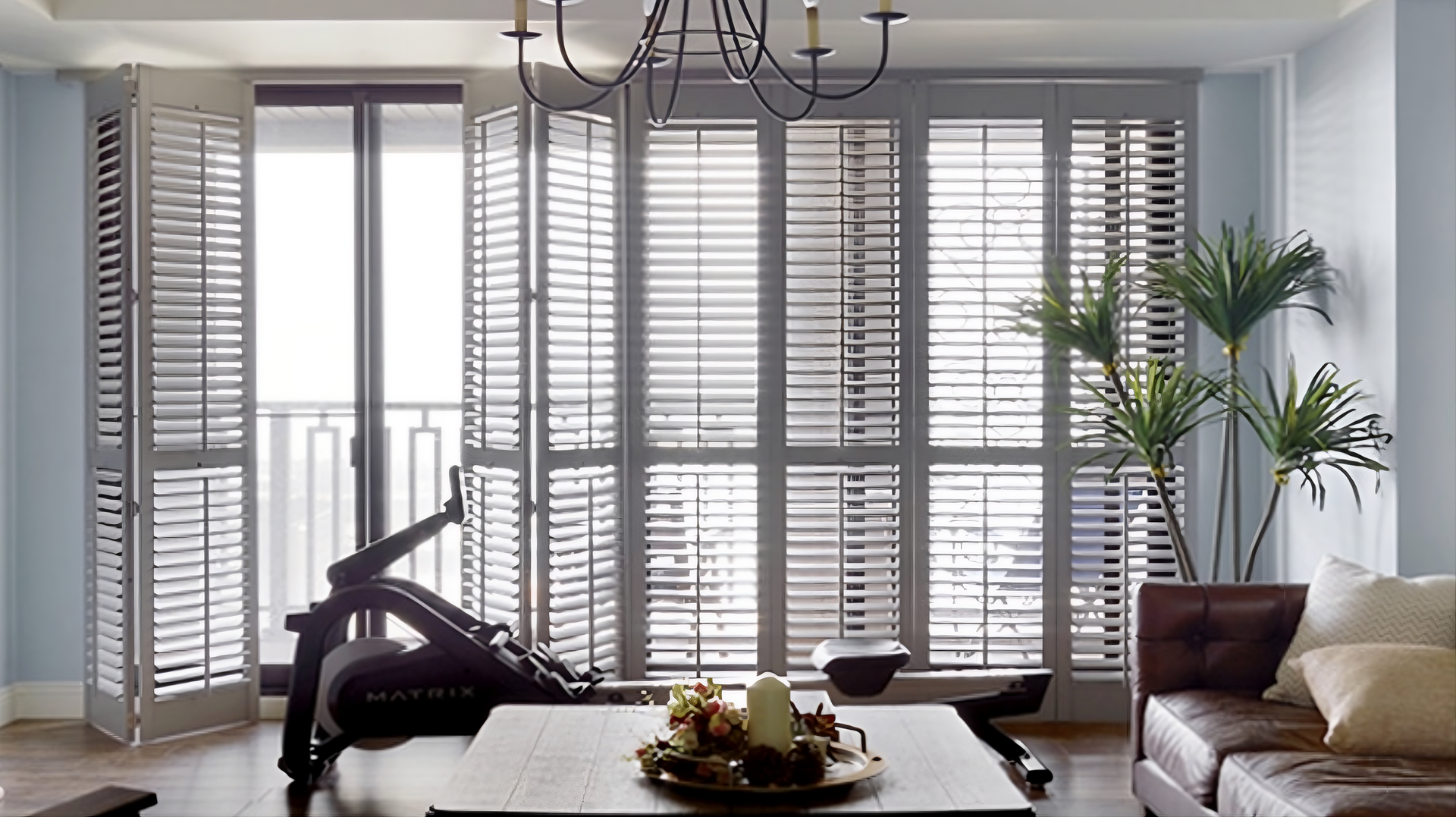 White interior shutters cover floor-to-ceiling windows and a sliding glass door in a living room.