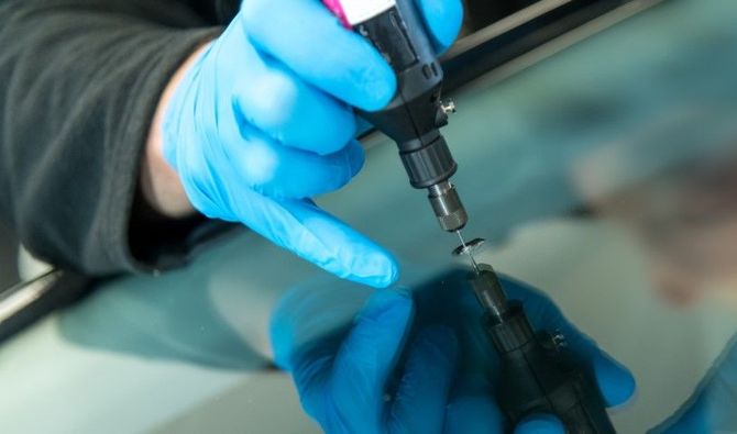 Blue-gloved hands applying liquid to a black device with a precision tool