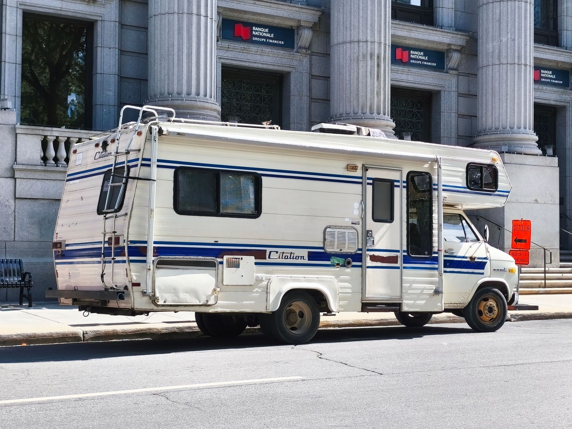 White RV parked on a city street in front of a stone building with columns