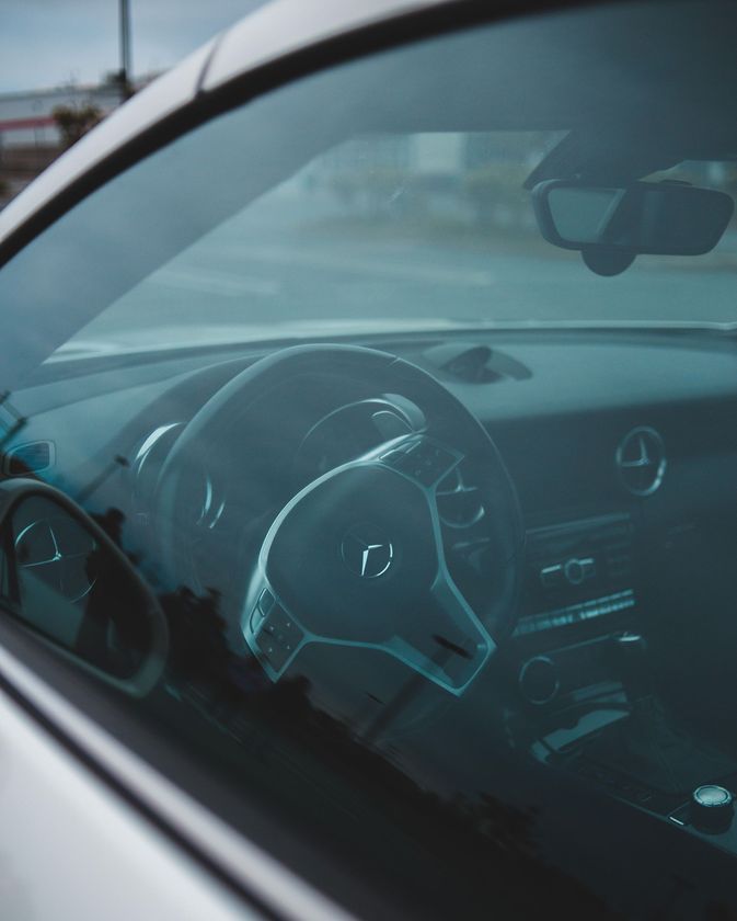 Steering wheel and dashboard seen through a car’s side window in a dim interior
