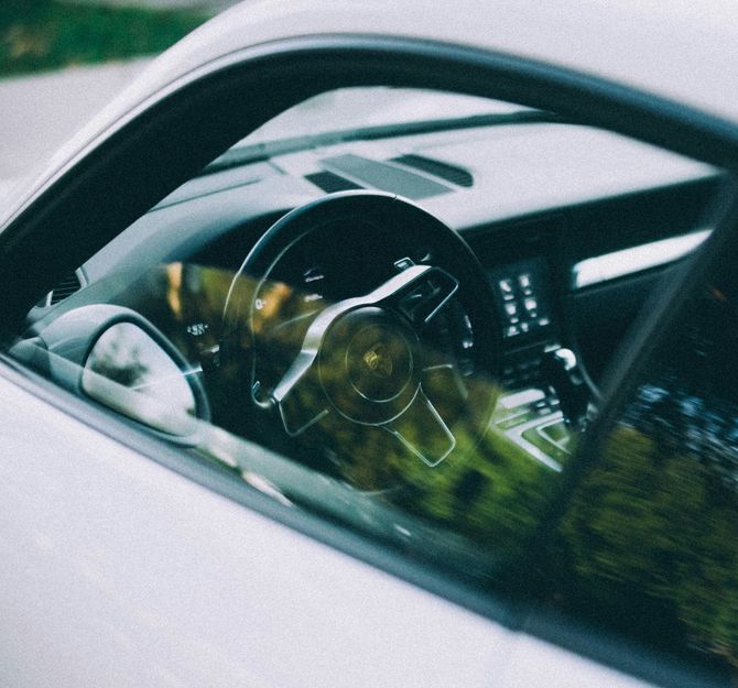 Steering wheel and dashboard seen through a car window with blurred greenery reflections