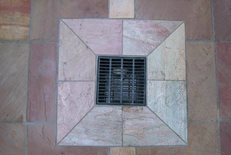 A Square Drain On A Tiled Floor With A Metal Grate — Leemark Design Services In Parramatta Park, QLD
