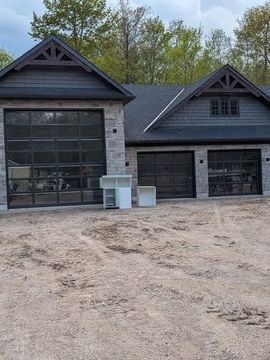 New house exterior with black garage doors, stone accents, and a gravel driveway