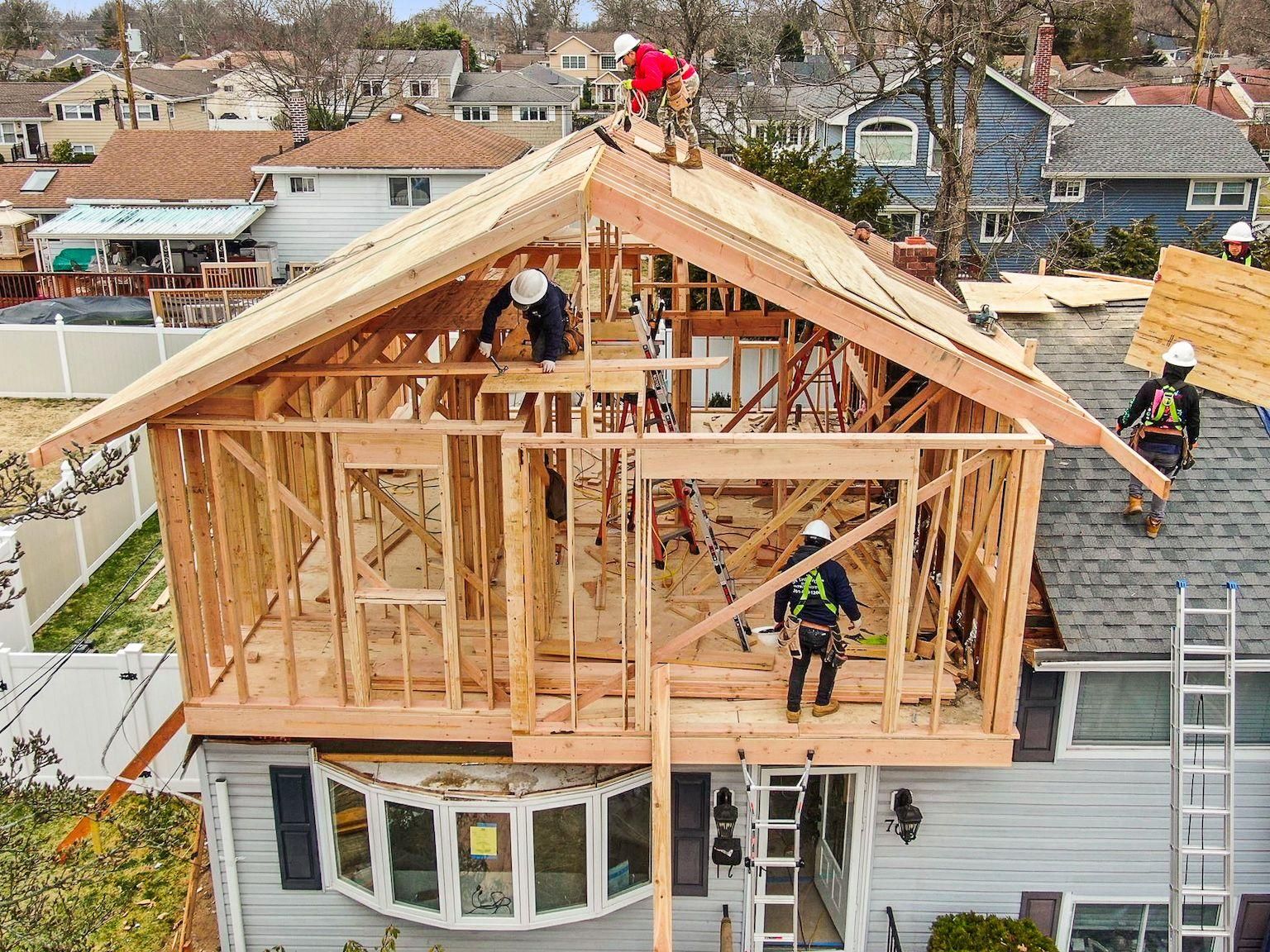 Roofers framing a house addition, with workers on the roof and upper floor