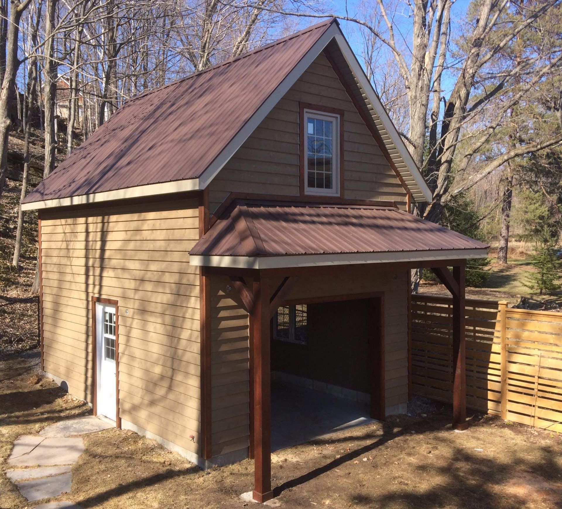 Small rustic wooden shed with a brown metal roof and open carport in a wooded yard