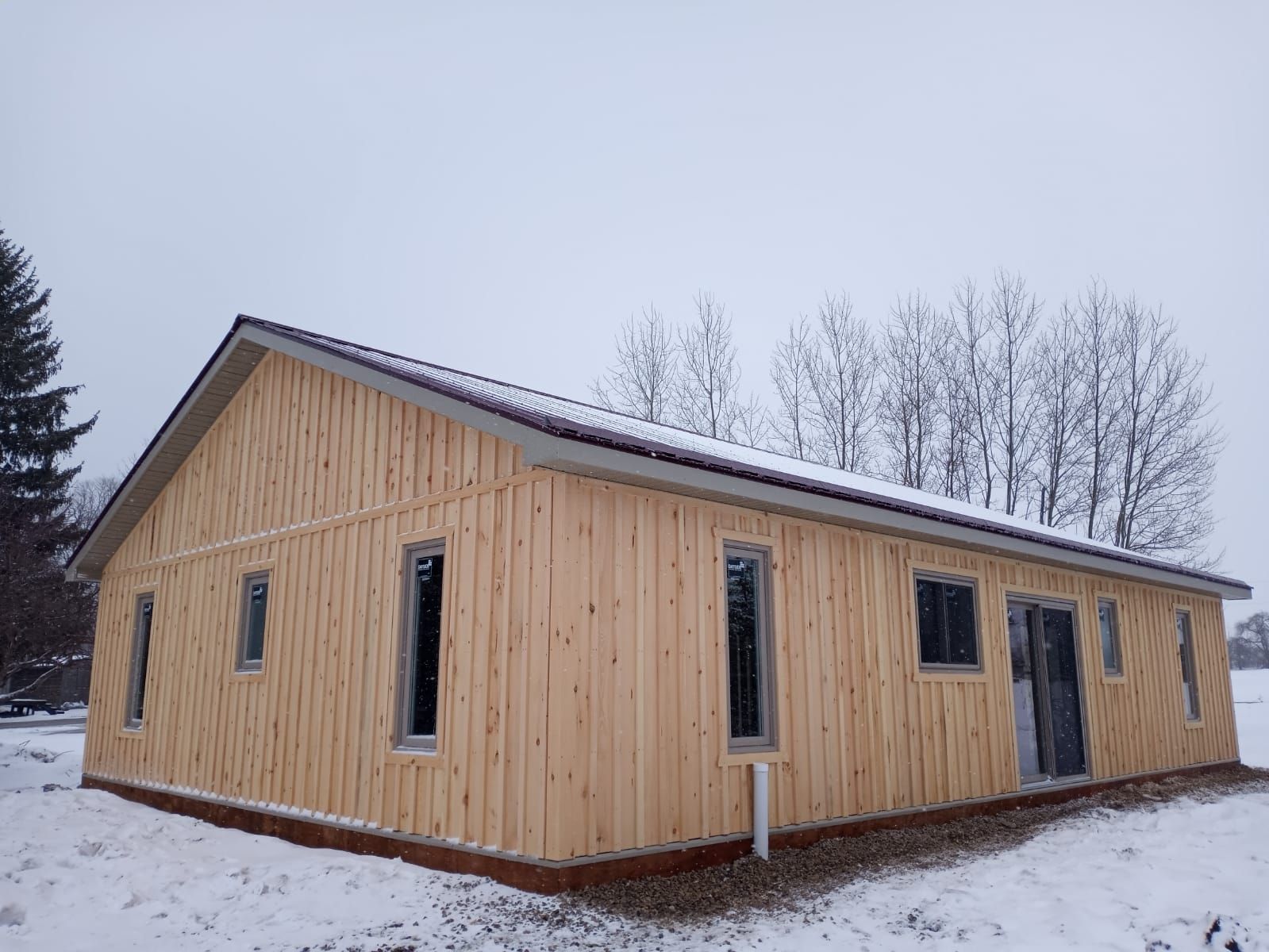 Wood-framed cabin under construction in a snowy landscape, with unfinished windows and a pitched roof