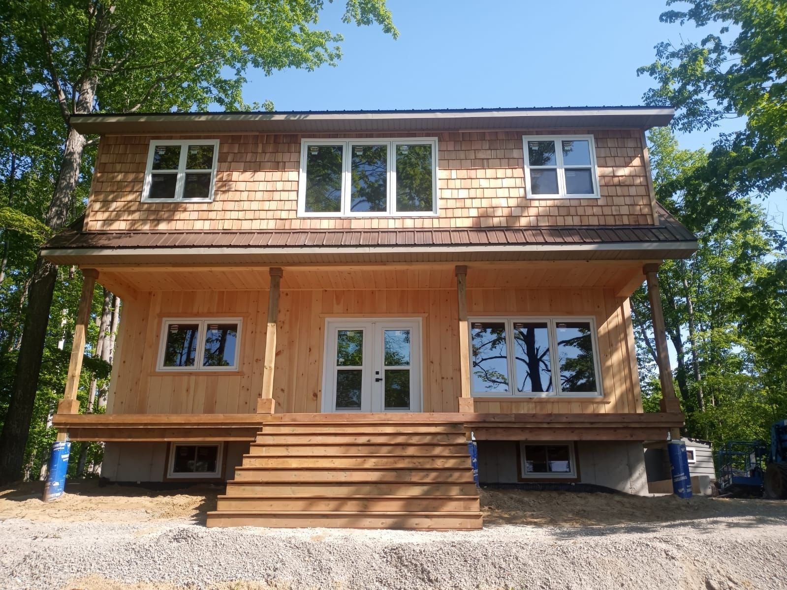 Two-story house under construction with wood framing, front steps, and trees around it
