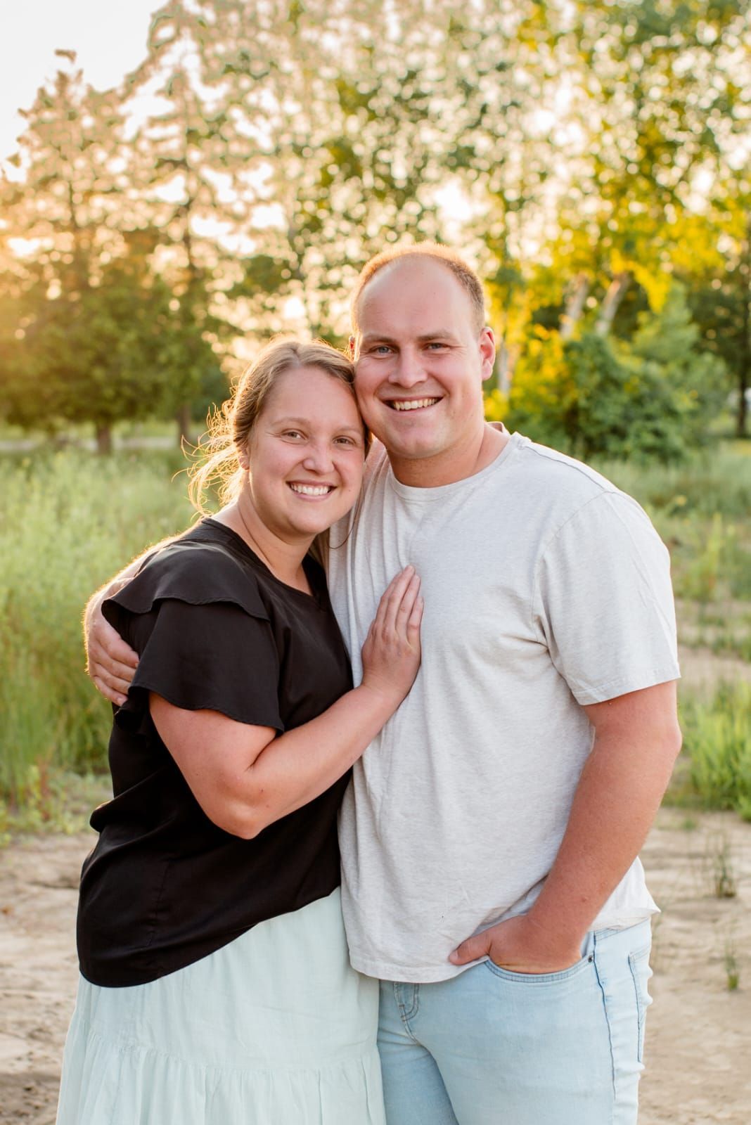 Smiling couple embracing outdoors at sunset, with trees and warm golden light in the background