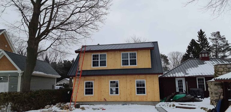 Yellow two-story house under construction with unfinished siding and snow in the yard