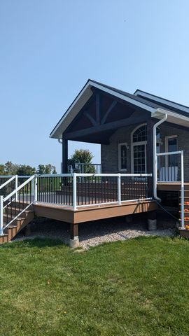 Small elevated porch with white railing, wooden deck, and stairs on a brick house under a blue sky