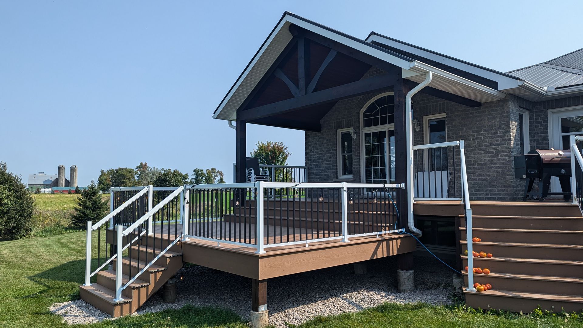 House porch with wooden deck, white railings, and stairs under a blue sky