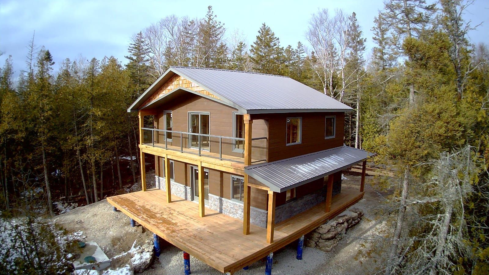 Two-story wooden house with snow-dusted roof in a forest clearing