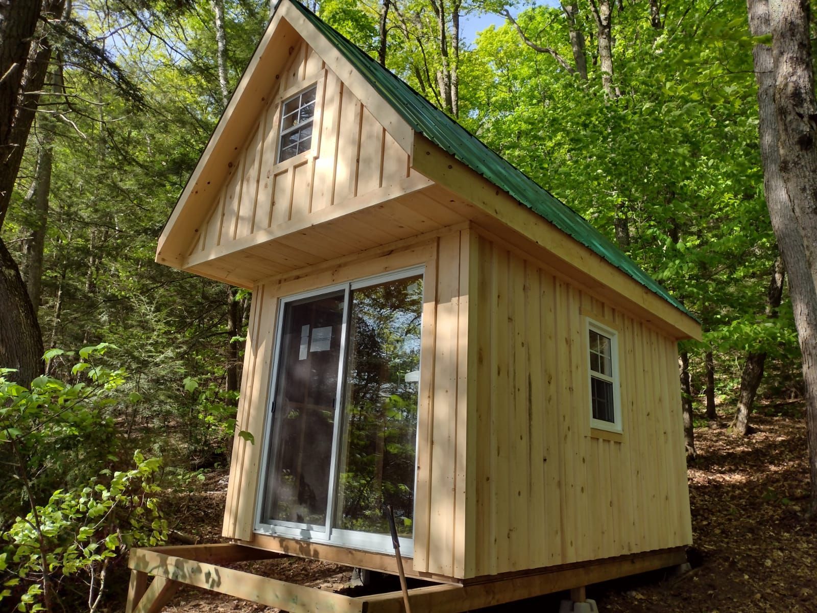 Small wooden cabin with a steep roof and sliding glass door in a wooded forest clearing