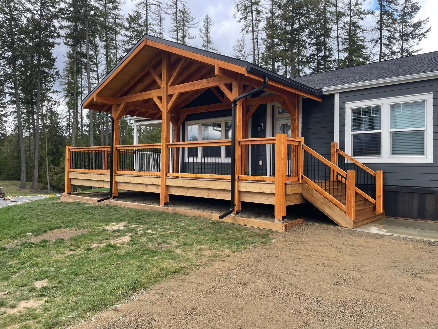 Wooden front porch with ramp and steps on a dark gray cabin in a wooded setting