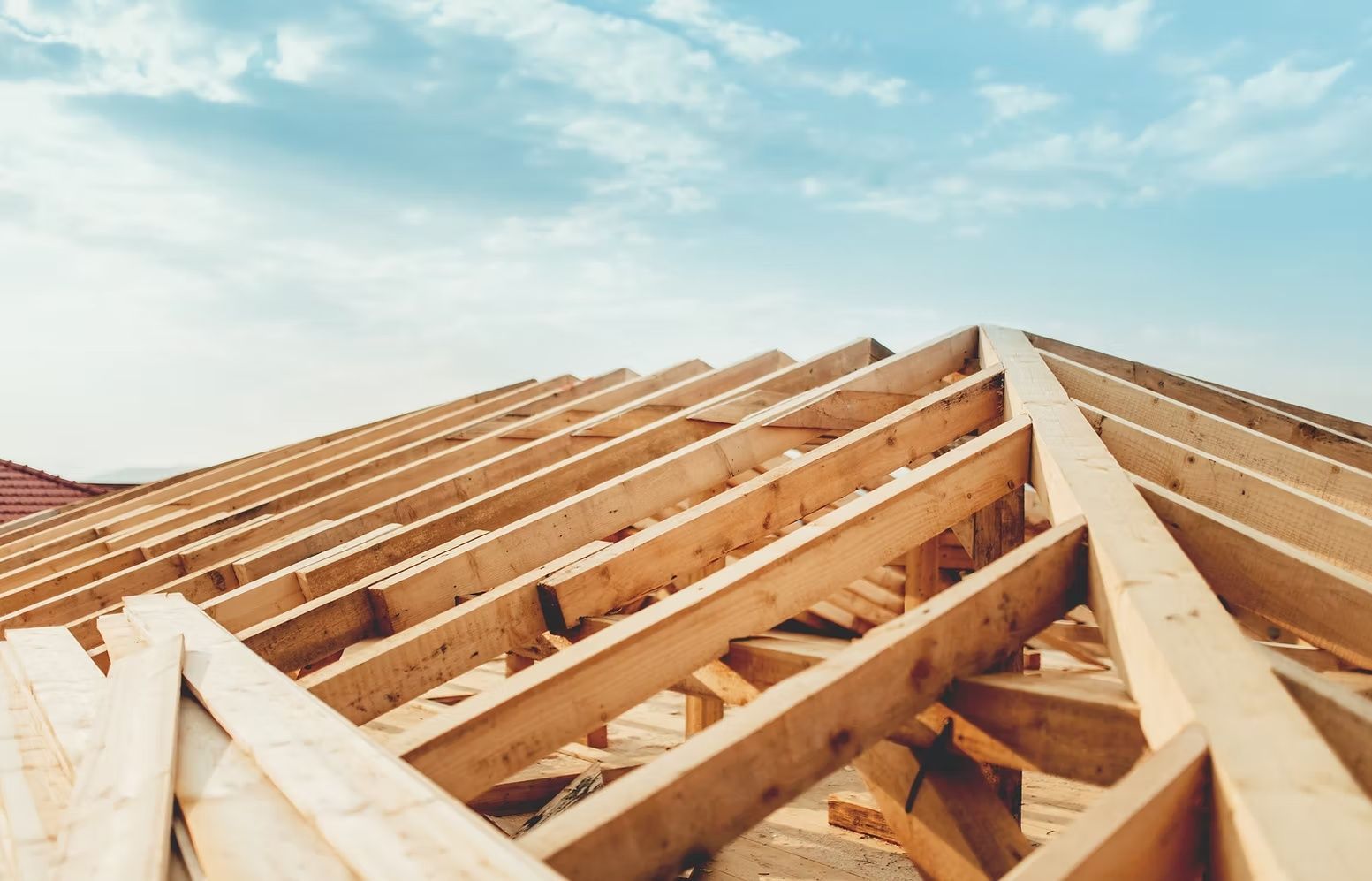 Wooden roof trusses under construction against a bright blue sky