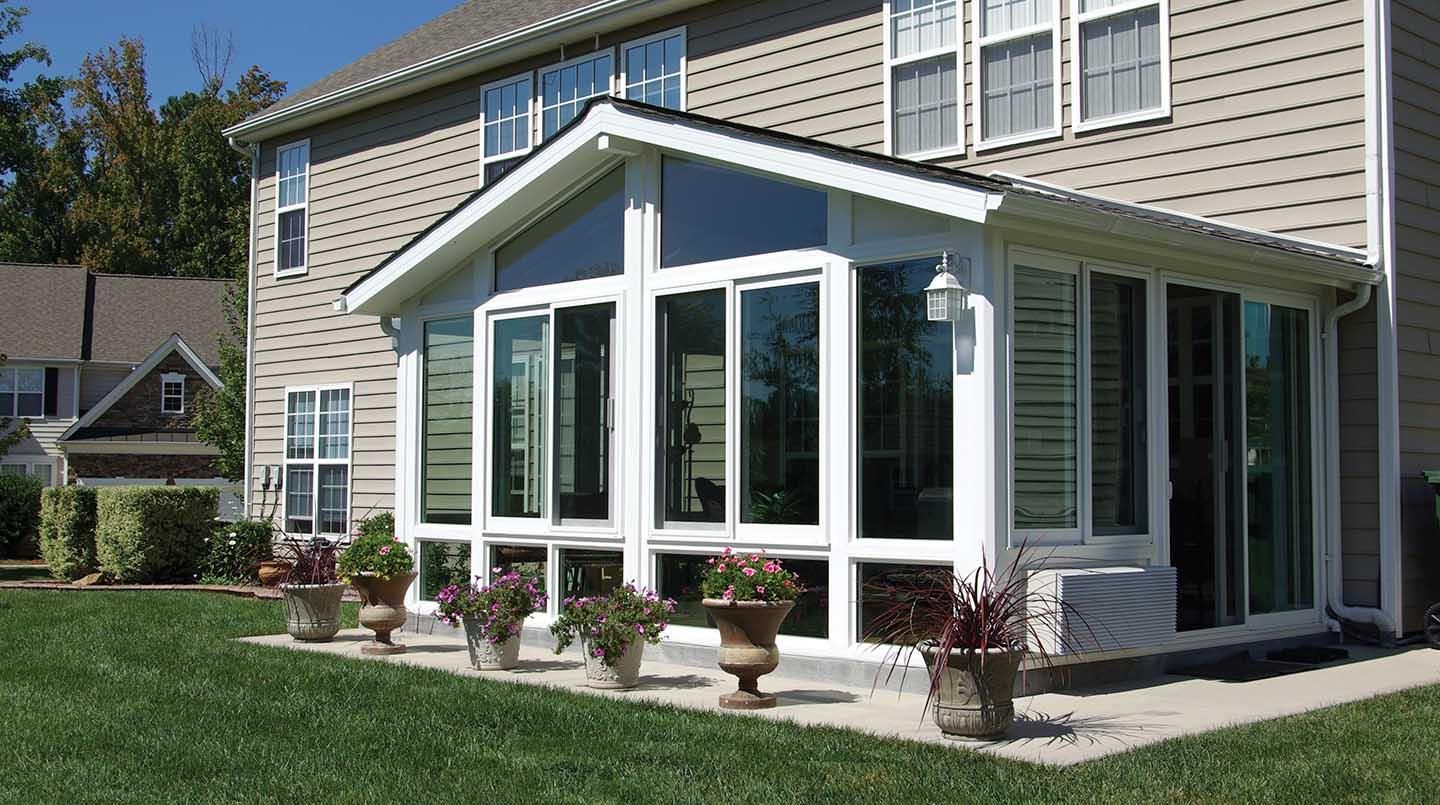 Sunroom addition with white-framed windows on a beige house beside a green lawn