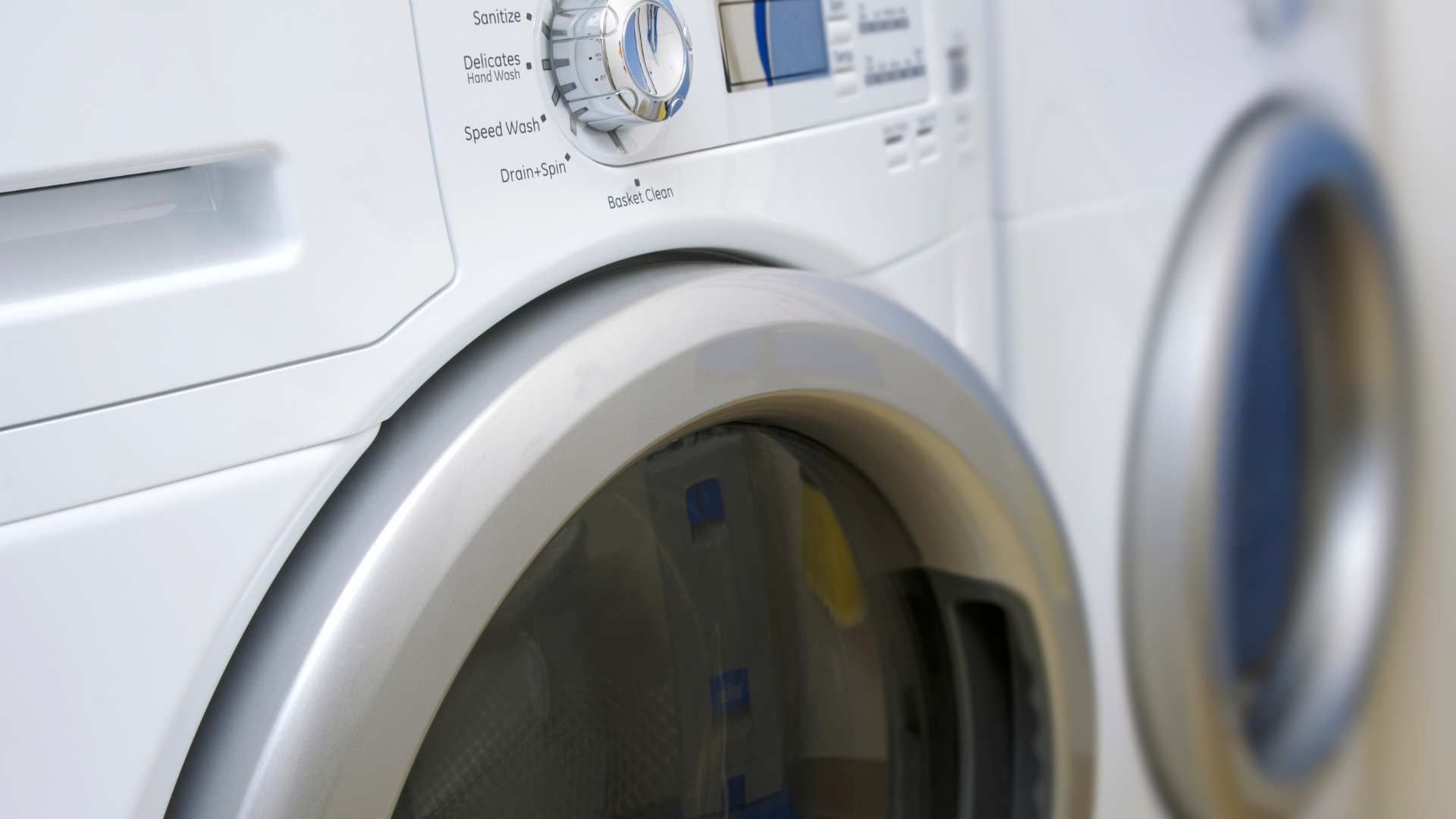 Front-loading white washing machines in a laundry room, one control panel in focus