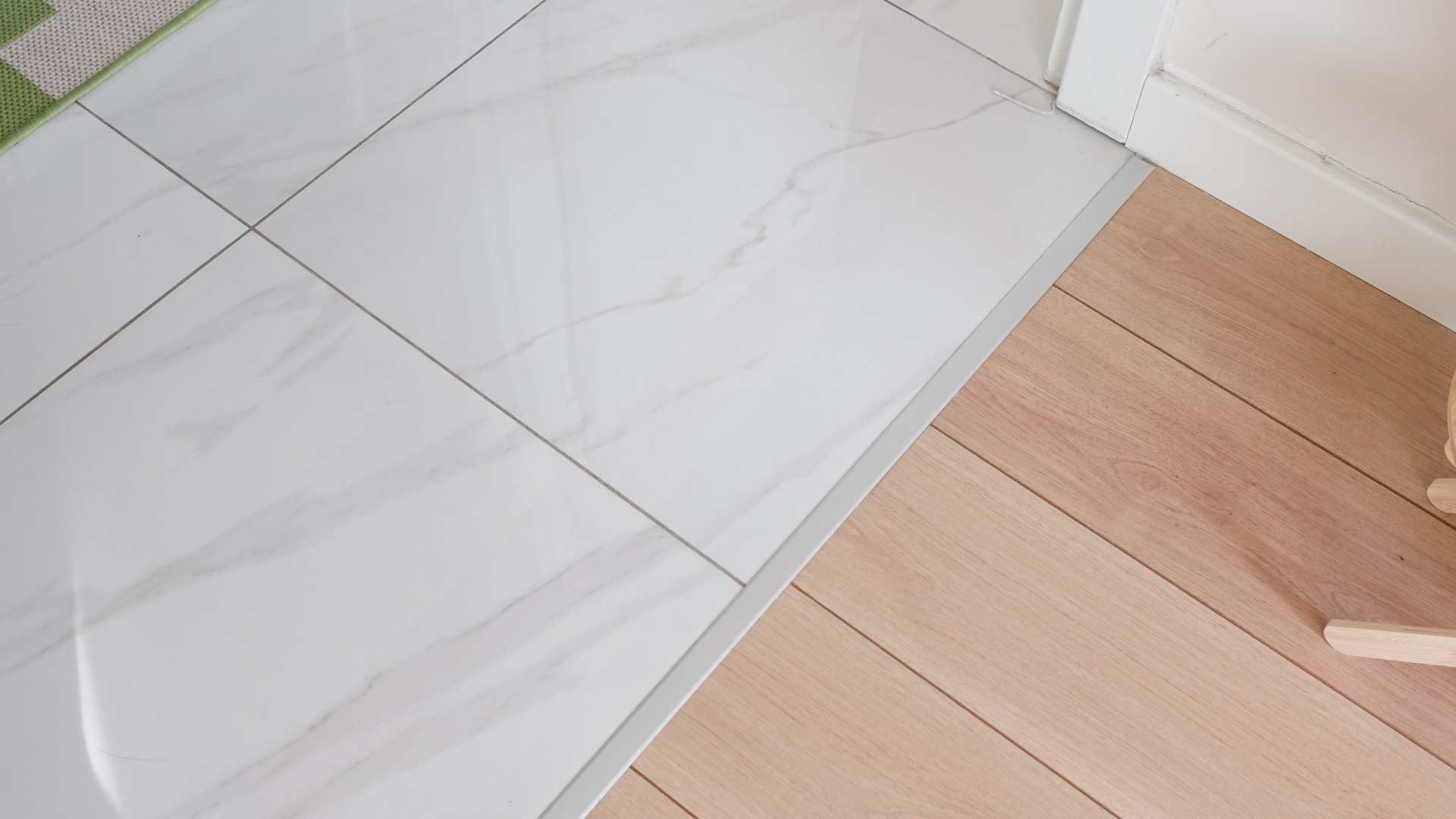 White tiled floor meets light wood flooring at a diagonal seam near a wall corner