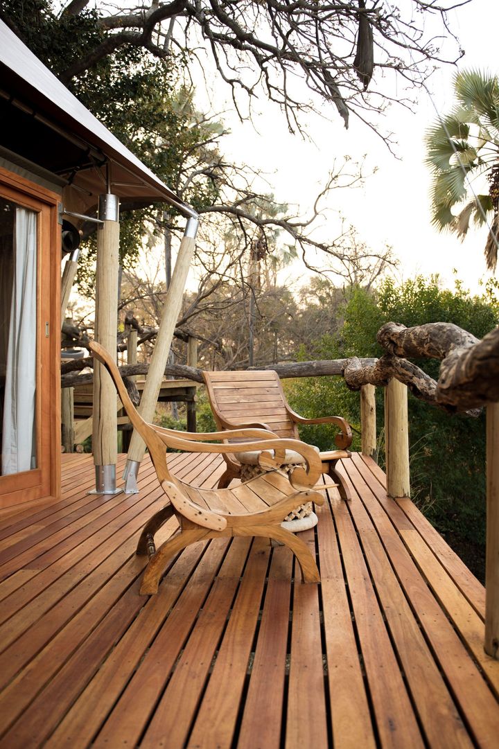 Wooden deck with lounge chairs beside a rustic cabin, overlooking trees at sunset
