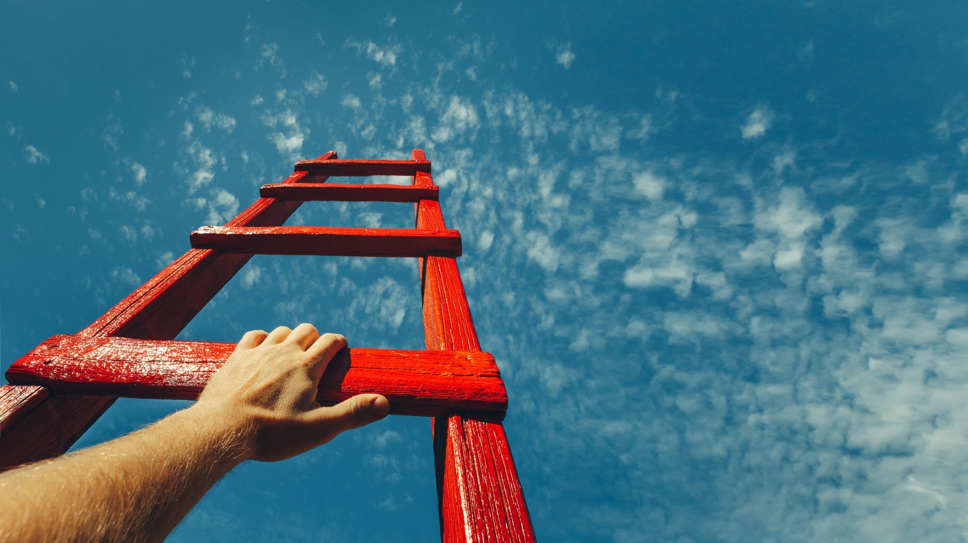 A person is climbing up a red ladder against a blue sky.