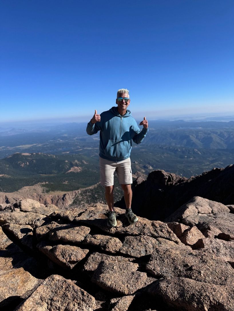 Picture of Coach David Berger in a hoodie and shorts on top of a mountain in Colorado.
