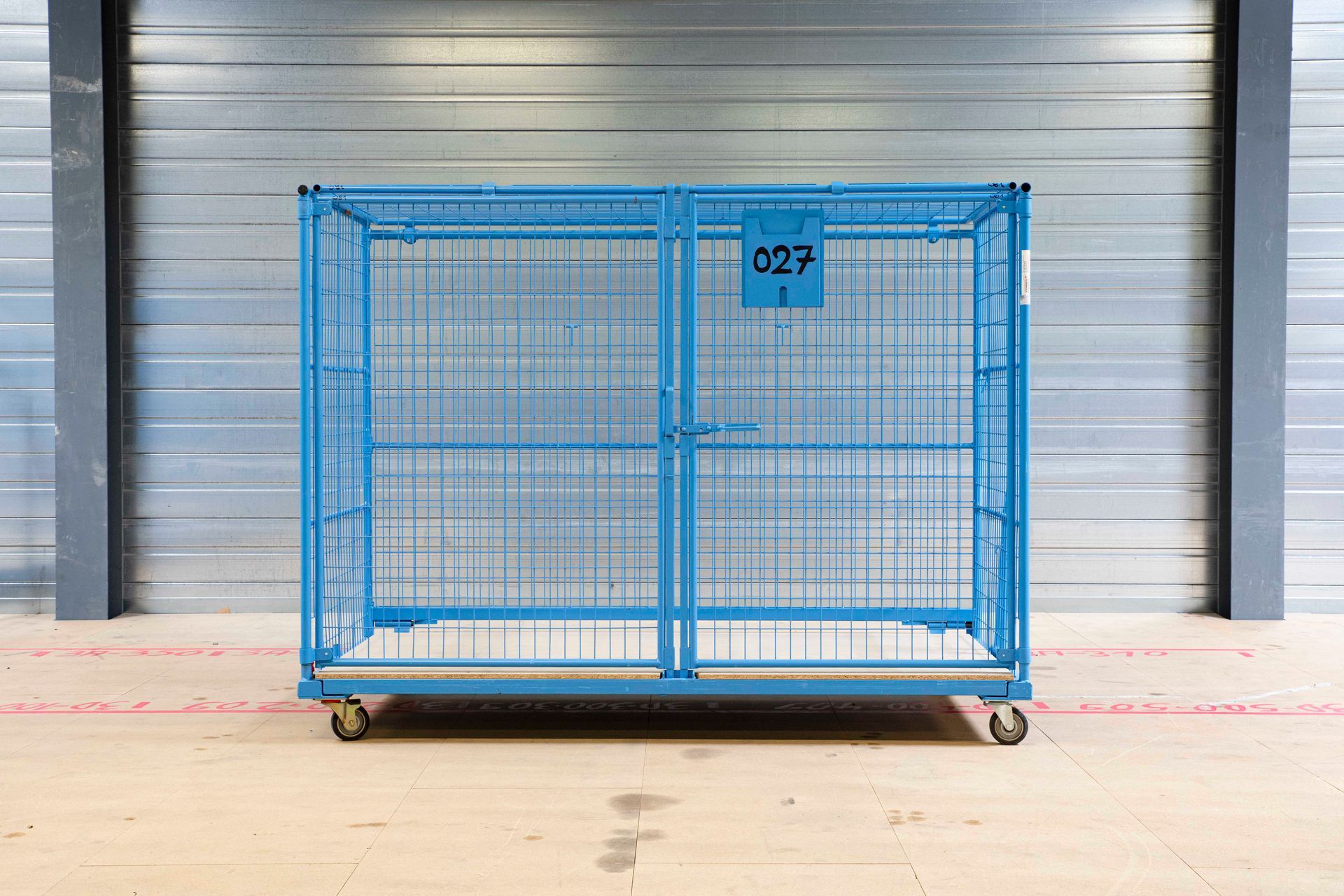 Vor der Tür einer Lagerhalle steht ein blauer Käfig mit Rädern.