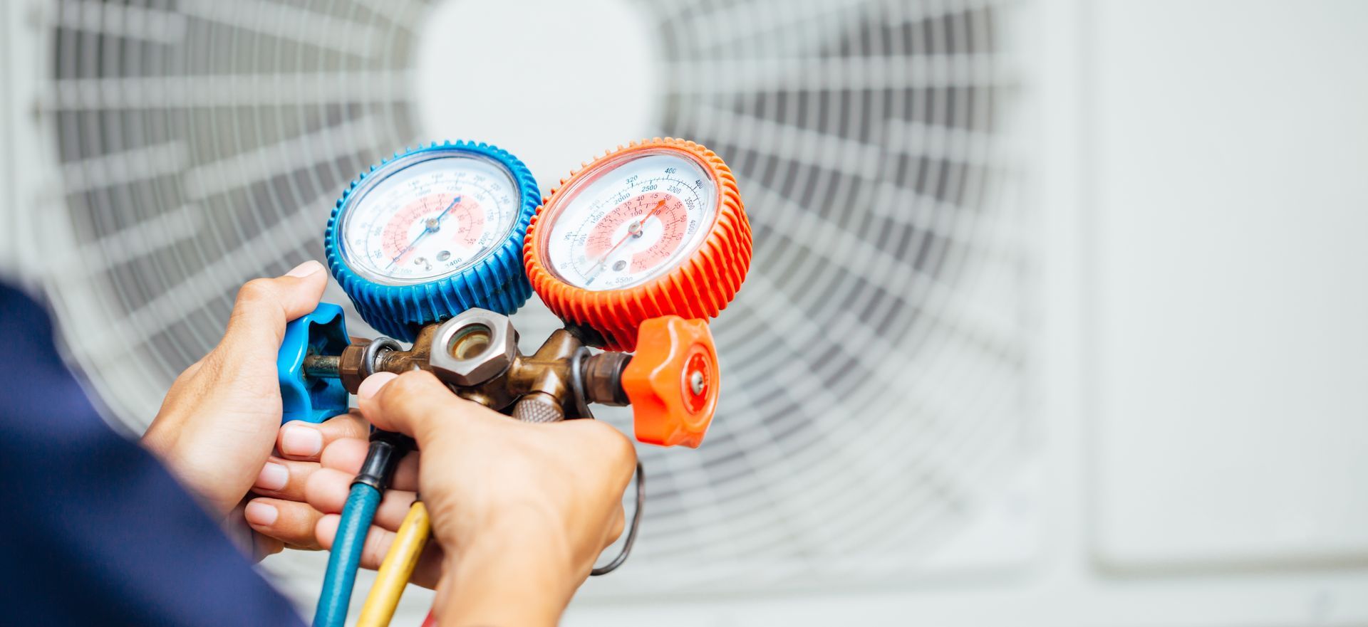 Hands holding HVAC gauges connected to an air conditioner unit outdoors