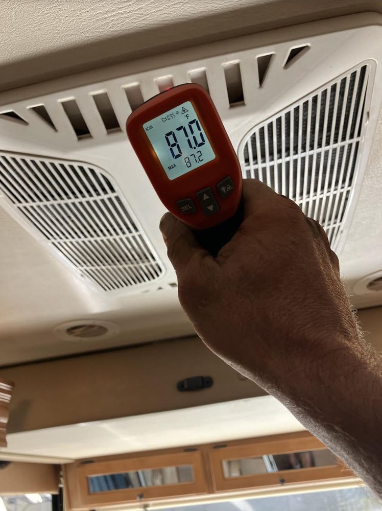 Hand holding a red infrared thermometer reading 81.0°F near a ceiling vent and air filter.