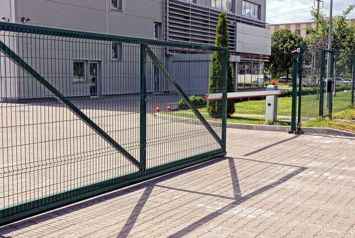 Cancello scorrevole in metallo verde, aperto, con un edificio sullo sfondo. Vialetto d'accesso in mattoni con barriera.