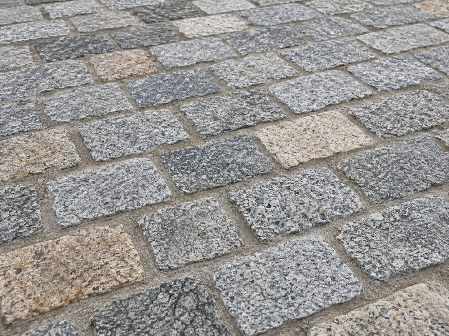 Close-up of grey and warm beige granite setts laid in staggered courses with neatly finished joints.
