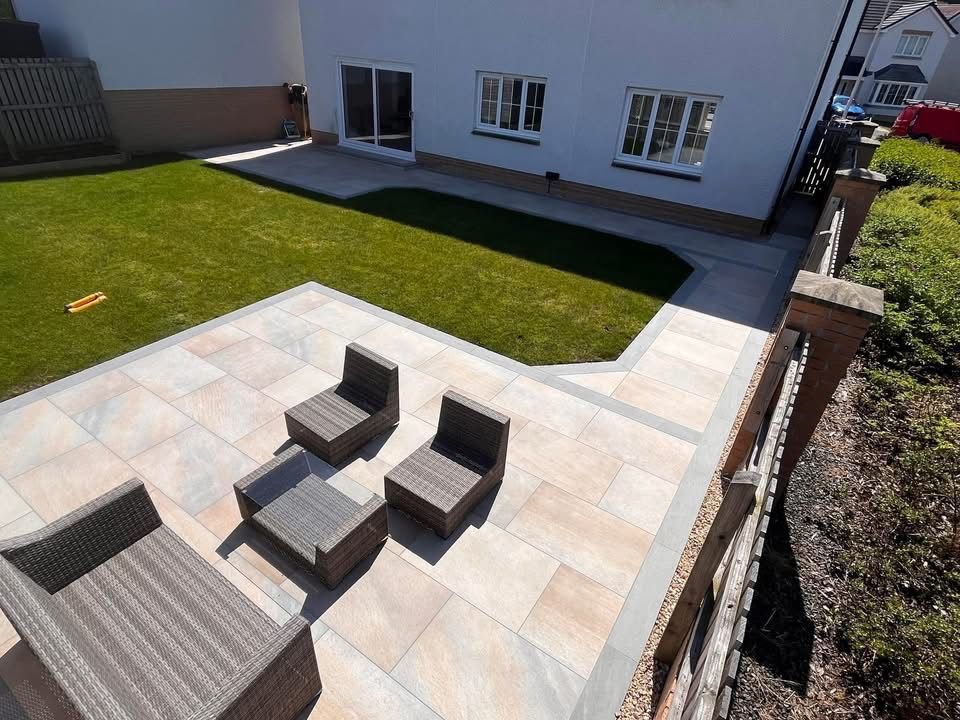Raised patio seating area in Glasgow with porcelain paving, garden furniture and neat lawn edging.