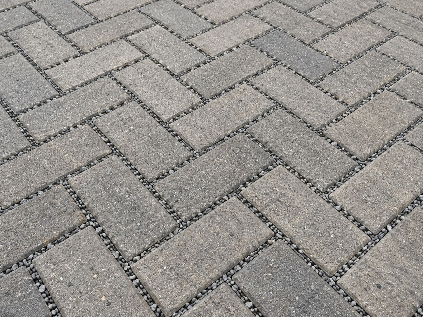 Close-up of grey herringbone block paving with stone-filled joints.