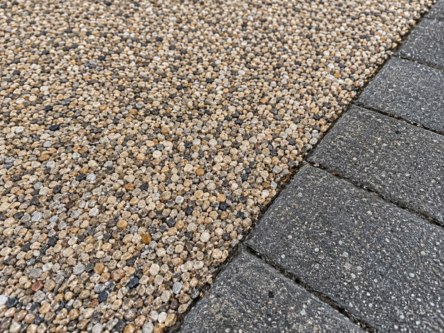 Close-up of buff and grey resin-bound aggregate beside charcoal block edging.