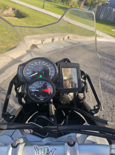 Vista del tablero y el parabrisas de una motocicleta de una carretera curva junto a un parque cubierto de hierba.
