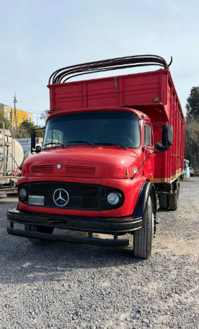 Camioneta Mercedes roja estacionada en un terreno de grava bajo un cielo despejado.