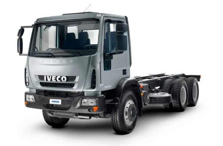 Camión volquete Iveco gris en un camino de tierra en una obra en construcción cerca de un edificio sin terminar al atardecer.