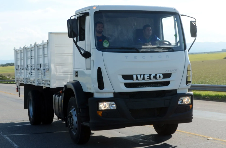 Camión Iveco blanco de plataforma plana circulando por una carretera en campo abierto.
