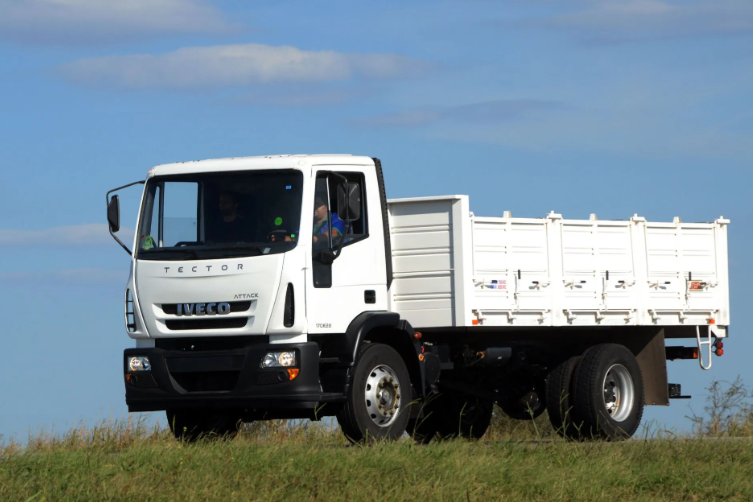 Camión Iveco blanco de plataforma plana circulando por una carretera en campo abierto.