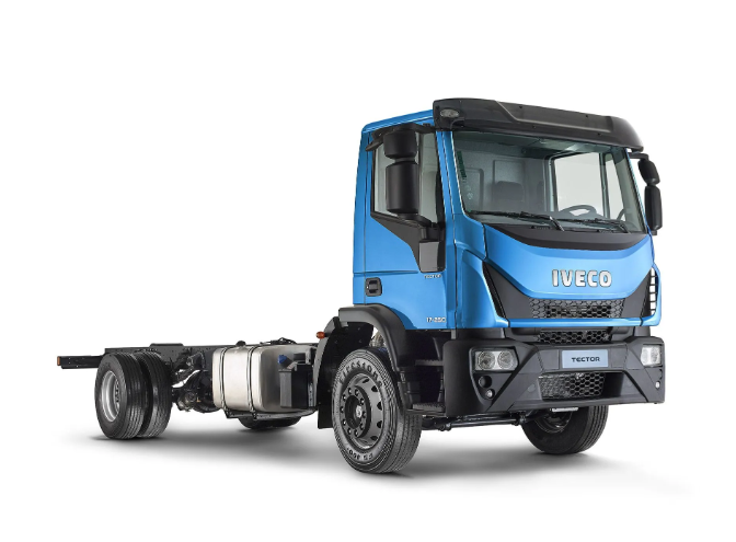 Camión de carga Iveco azul circulando por una carretera junto a un almacén moderno.