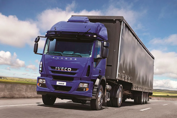 Un camión semirremolque Iveco morado circula por una autopista con un remolque negro.