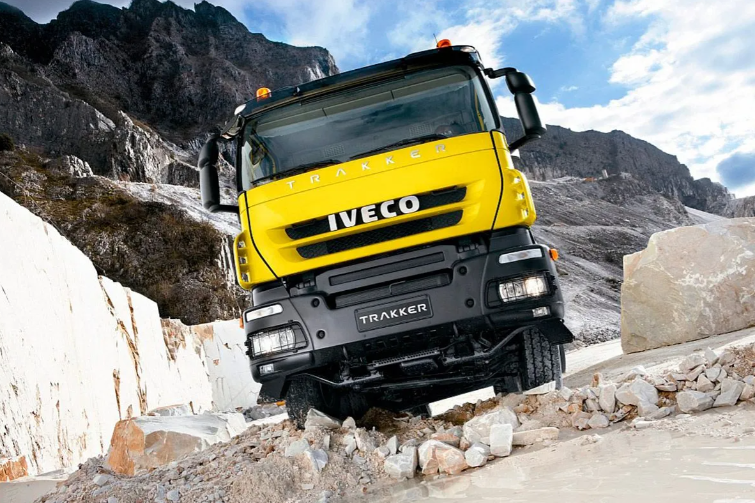 Un camión volquete Iveco amarillo recorre un sendero rocoso de una cantera, inclinado entre muros de piedra.