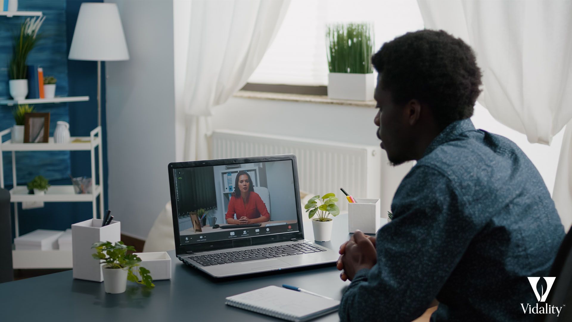 A man sitting at a desk with a laptop open, engaged in a video call.