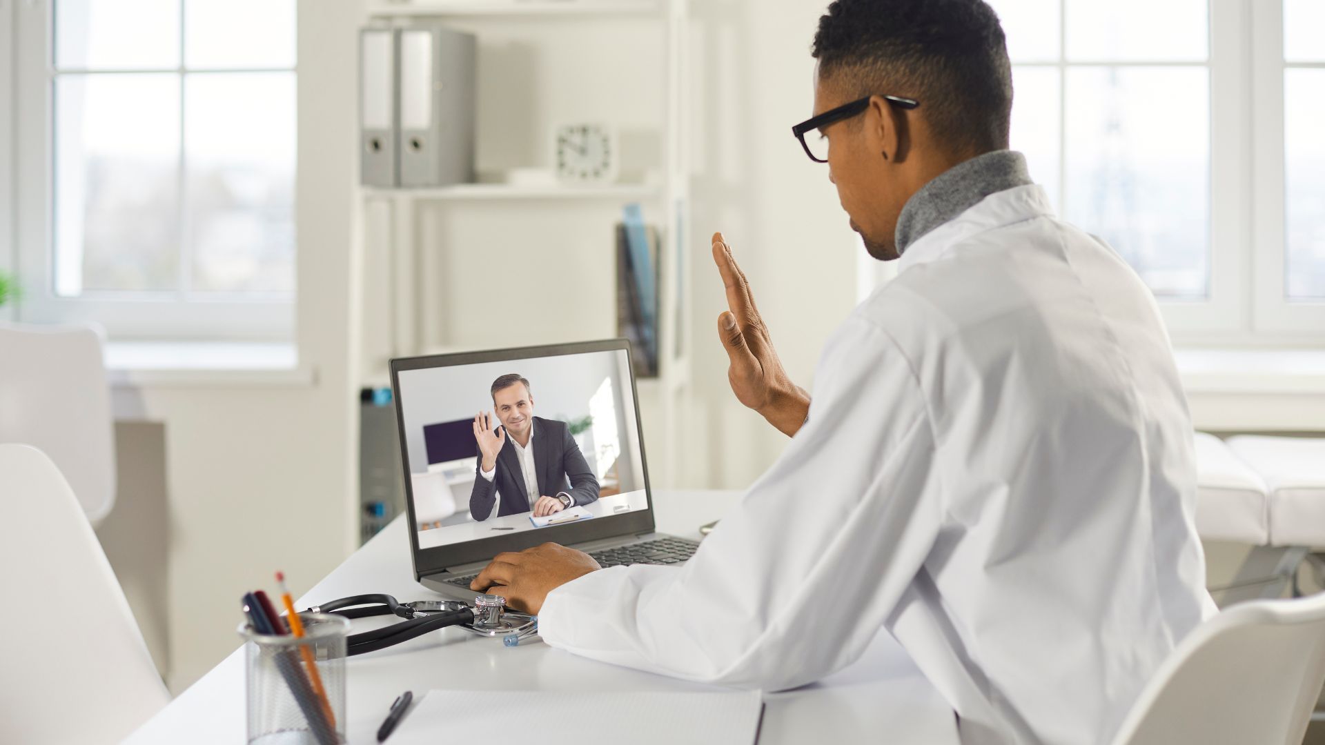 A man in a white coat sitting at a desk with a laptop, focused on his work.
