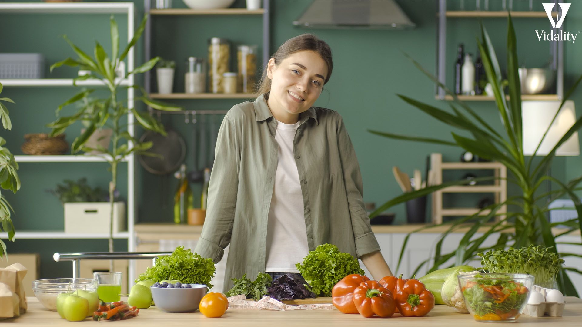 A woman happily stands in front of a table filled with fresh vegetables.