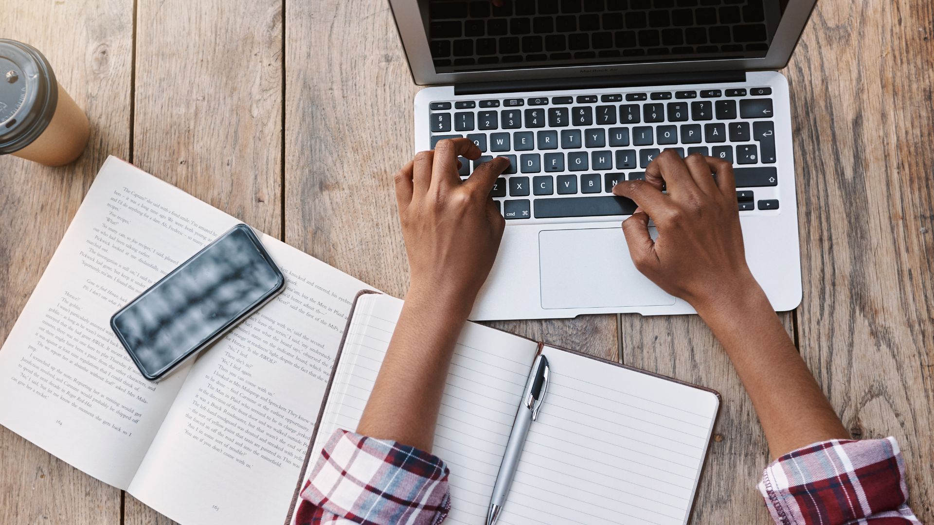 Woman's hands typing on laptop with coffee cup nearby.
